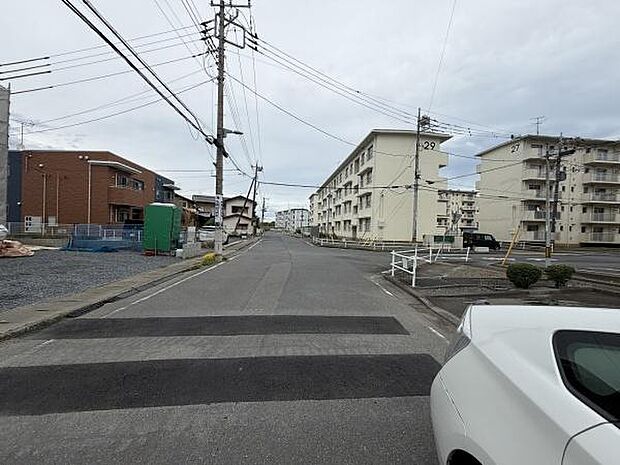 現地前面道路は広く交通量も落ち着いた印象です。周辺にはマンションが建ち並んでおり生活利便施設も近隣に整っています。歩道やガードレールも設けられており安心感があります。