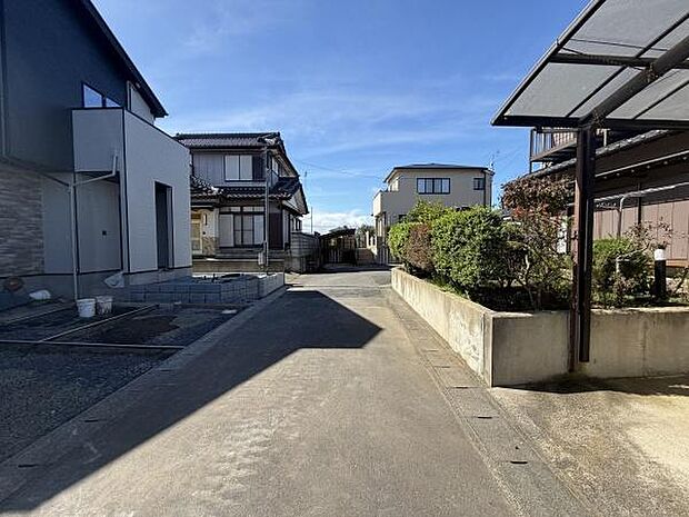 前面道路が広がり車の出入りもスムーズに行えます。陽当たりの良い現地写真で周囲には落ち着いた住宅が並びます。道路沿いに緑が配置されており視界も開けています。清潔感のある舗装道路が印象的です。