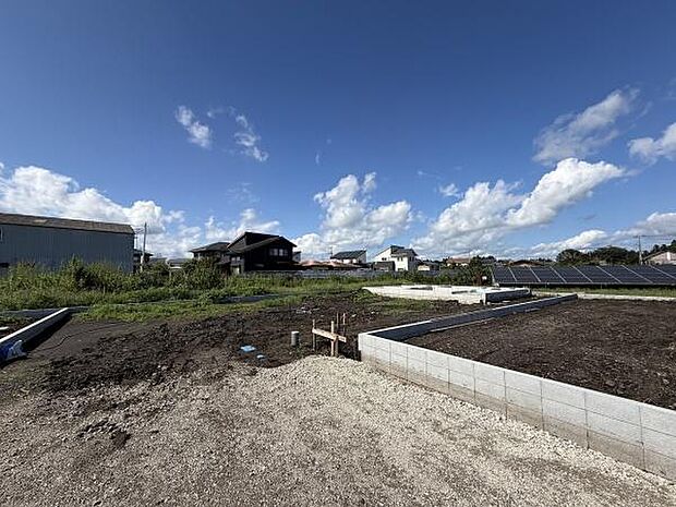 青空が広がる景色が開放的な印象を与えます。敷地内の様子も分かりやすく周囲の住宅やソーラーパネルも確認できます。自然を感じられる落ち着いた環境です。建築の準備が進んでいる様子がうかがえます。