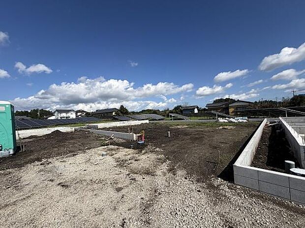 広々とした敷地で開放感があります。周囲には住宅や自然豊かな景色が広がっています。日当たりも良好な土地です。基礎工事が進行中の新築現場です。様々なプランに対応できる立地です。