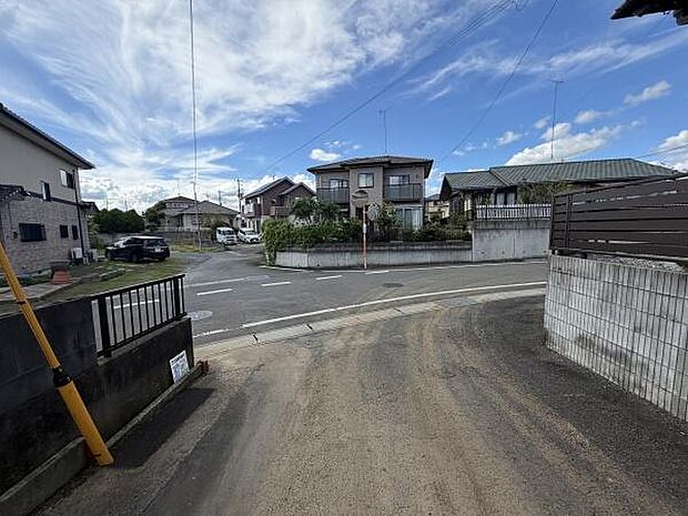 落ち着いた住宅街に位置している現地写真です。前面道路は車の往来が見えやすく見通しの良い環境です。通り沿いの住宅も手入れされており周辺の雰囲気が伝わってきます。空の広がりも感じられるロケーションです。