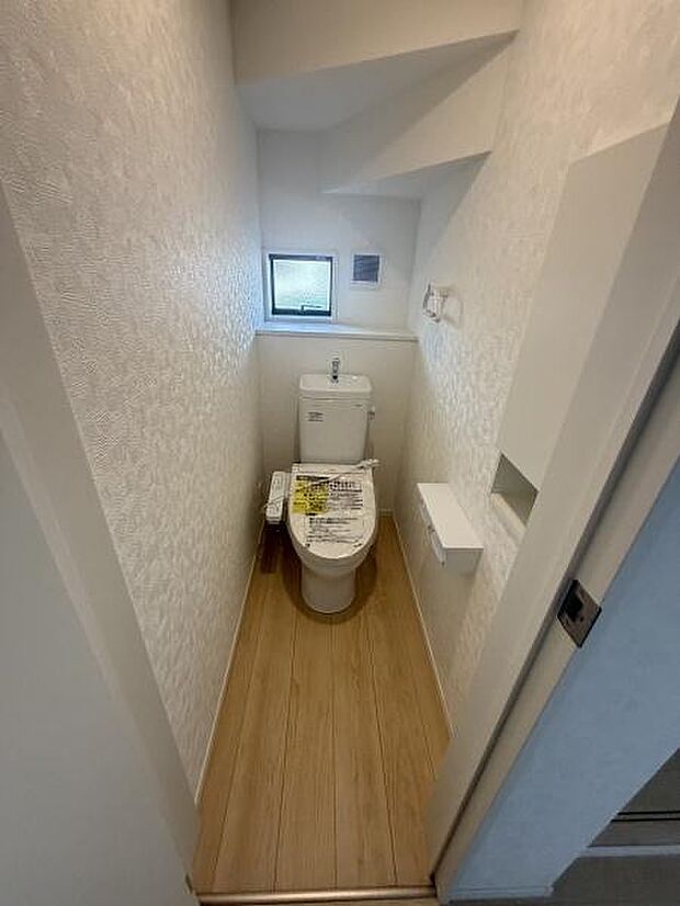 明るさを感じる窓付きのトイレです。コンパクトにまとまった設計でお掃除も便利な印象です。床材は木目調で落ち着いた雰囲気があります。ペーパーホルダーや収納スペースも確保されています。