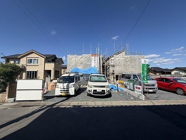 新しい建物が建設中の現場です。青空が広がり周辺には住宅が並んでいます。複数台の車が駐車できるスペースがあります。整然とした環境が感じられます。