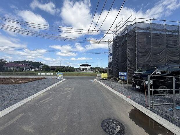 前面道路は幅がしっかり確保されており車の出入りにも余裕があります。周囲は開放感があり空が広く感じられる環境です。舗装された道路と整然とした敷地が印象的です。建築中の現地の様子もしっかりと確認できます。