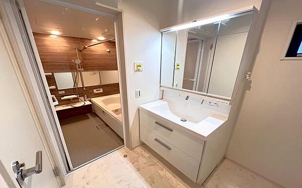 《洗面化粧台》　■洗面化粧台の鏡は、メイクや髭剃りに便利な三面鏡タイプ。開いて合わせ鏡としても使用できます。鏡の裏側は収納スペースとして利用でき、小物などの保管に便利な棚も付いています。