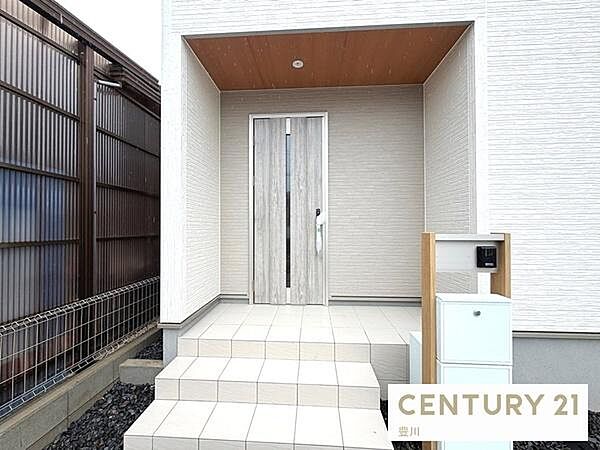 木目調の軒天がおしゃれな玄関ポーチ。ステップ付きのタイルアプローチに加え、インターホンとポストが一体となったモダンな機能門柱が設置されています。