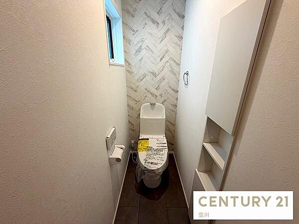 1Fトイレは、清潔感のあるホワイトと木目調のアクセントクロスがおしゃれな空間。小窓付きで自然光が差し込み、明るい雰囲気です。背面の壁面収納は小物の収納に便利。快適に過ごせる温水洗浄便座仕様です。