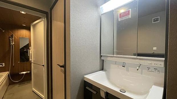 《洗面化粧台》　■洗面化粧台の鏡は、メイクや髭剃りに便利な三面鏡タイプ。開いて合わせ鏡としても使用できます。鏡の裏側は収納スペースとして利用でき、小物などの保管に便利な棚も付いています。