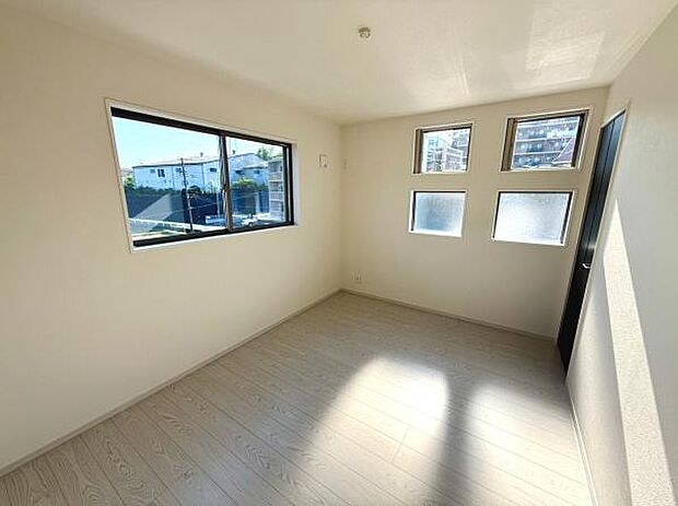 大きな窓から自然光がたっぷり差し込む洋室です。シンプルな内装でレイアウトの自由度が高い空間です。四角い小窓がアクセントとなり明るさと開放感を演出しています。落ち着いた雰囲気の床材も特徴です。