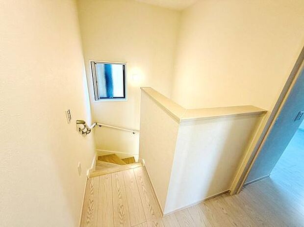 明るい光が差し込む階段スペースです。手すり付きで安心感があります。窓が設置されており通風や換気にも配慮されています。開放感のある空間設計が印象的です。