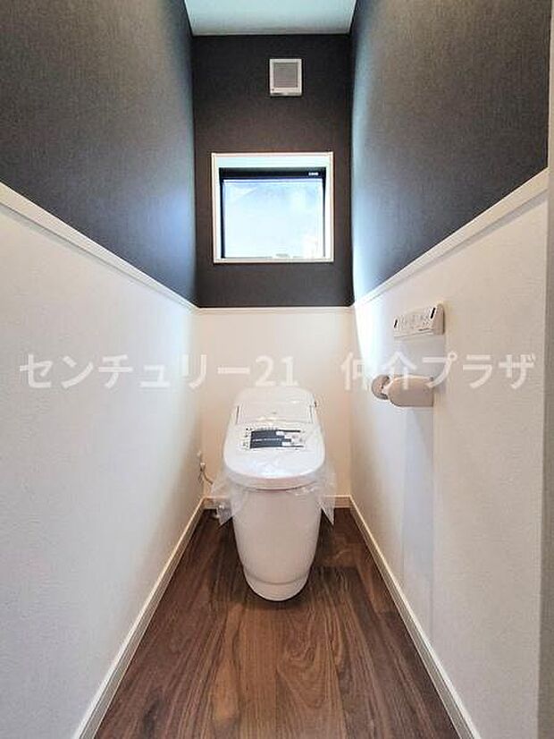 洗練されたデザインのトイレで清潔感が漂います。窓から自然光が差し込み明るい空間を演出します。ダークトーンの壁が落ち着いた雰囲気を醸し出しています。フローリングの床が高級感を添えています。
