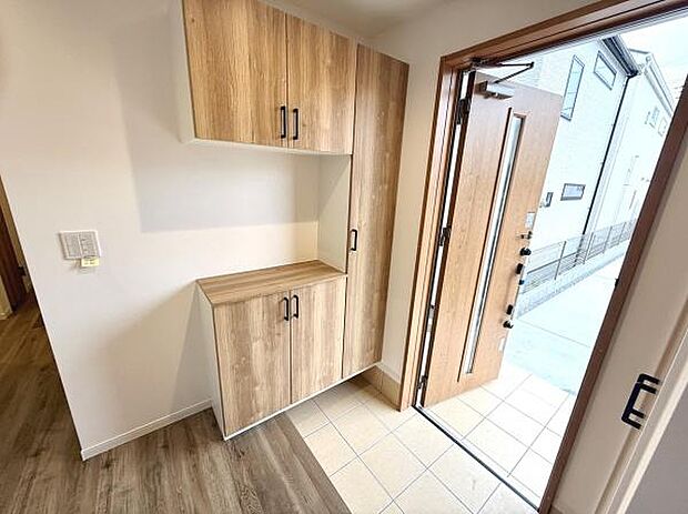 玄関には木目調の収納スペースが備わっておりすっきりとした空間を演出します。明るいタイル床が印象的でナチュラルな雰囲気が際立ちます。玄関扉は採光窓付きで自然光が入りやすい設計です。