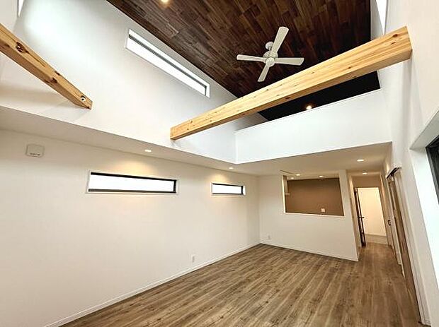 吹き抜け天井が開放感を演出しています。木目調のフローリングと天井が温かみを感じさせます。スリット窓からやわらかい自然光が差し込みます。梁のアクセントが個性的な雰囲気をプラスしています。