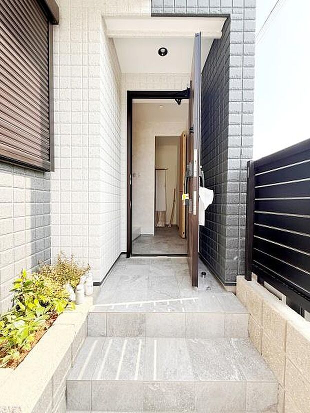 明るいタイルが印象的な玄関です。段差がゆるやかで出入りしやすい設計です。植栽スペースがアクセントとなり外観に彩りを加えています。門扉から玄関までの動線がスムーズです。