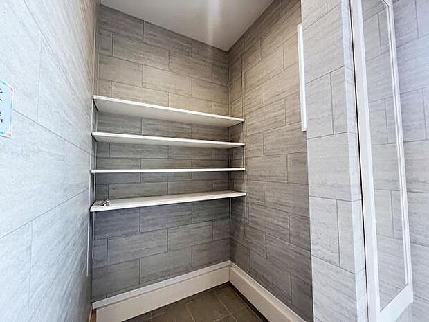 玄関スペースに設けられた棚が特徴的です。すっきりとしたタイル調の壁が印象的でシンプルなデザインが魅力的です。明るい照明が空間全体をしっかりと照らしています。便利な収納棚で整理がしやすいです。
