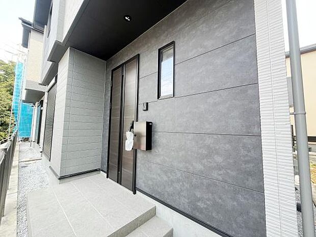 スタイリッシュな外観の玄関が印象的です。玄関扉がモダンなデザインで住まい全体の雰囲気を高めています。タイル張りのアプローチが清潔感を演出します。ポストやインターホンもシンプルにまとまっています。