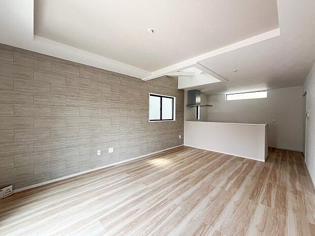 ナチュラルな床材が明るい印象を与えます。キッチンとリビングが一体化したレイアウトです。アクセントウォールが空間の印象を引き締めています。天井のデザインがすっきりとした雰囲気を演出します。