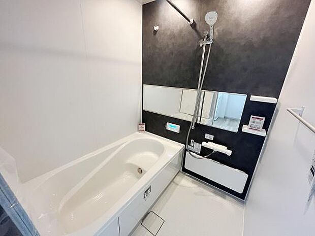 シンプルな色合いのバスルームです。大きめのミラーが設置され開放感があります。壁面にはアクセントカラーが施され空間にメリハリを与えています。バスタブは使いやすい形状です。