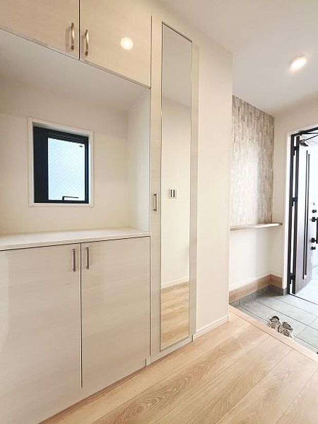 明るい玄関スペースが広がり清潔感のあるデザインが印象的です。大きな鏡付きの収納が便利です。窓から差し込む自然光で全体がより開放的に感じられます。扉横のタイルもアクセントになっています。