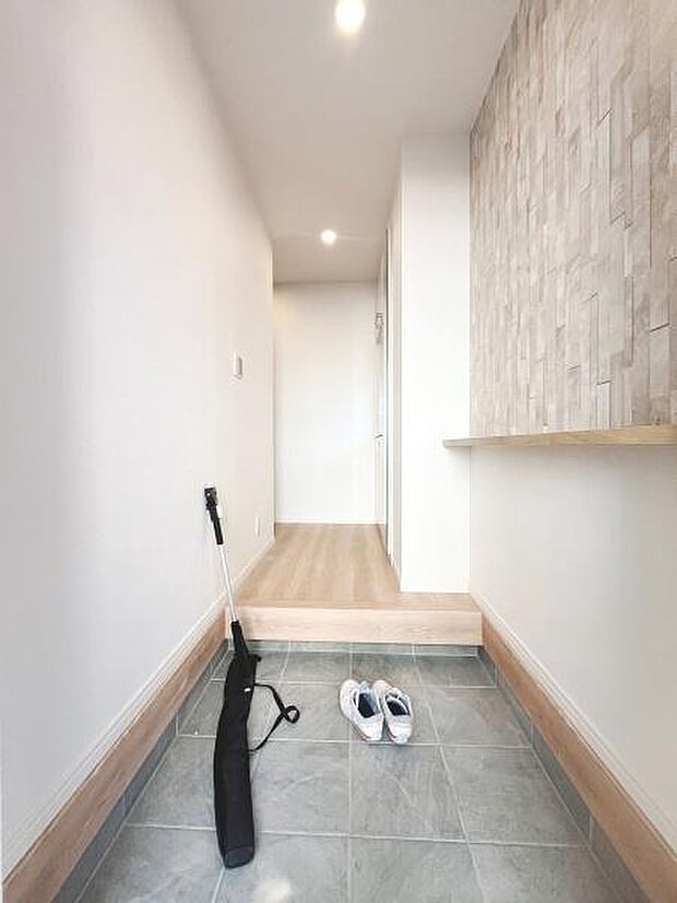 明るい照明が印象的な玄関です。広々とした空間で清潔感のあるタイル床が特徴です。壁面のデザインもアクセントになっています。段差があり使い分けしやすい設計です。収納や荷物の仮置きにも便利です。
