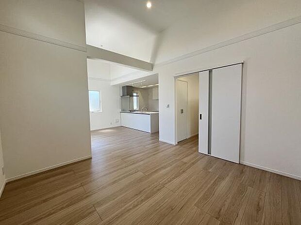 リビングは白を基調とした明るい空間です。天井が高く開放感があります。床の木目調が落ち着いた雰囲気を演出しています。キッチンエリアへの動線もシンプルです。引き戸で空間を仕切ることができます。