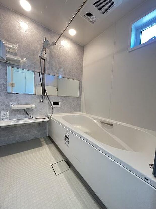シンプルなデザインのバスルームです。バスタブと洗い場がゆったりと配置されています。明るい照明と小窓が空間に開放感をもたらしています。壁面には便利なミラーが設置されています。