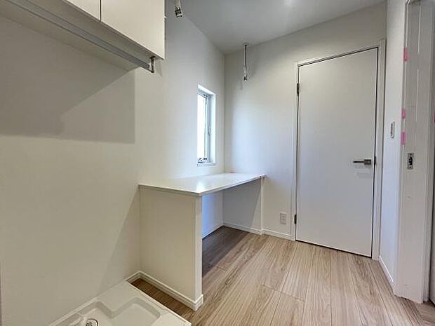 シンプルなデザインで清潔感がある洗面所です。ナチュラルな床が空間を広く見せます。窓から自然光が入り明るさが確保されています。収納棚も設置されており使い勝手に配慮されています。