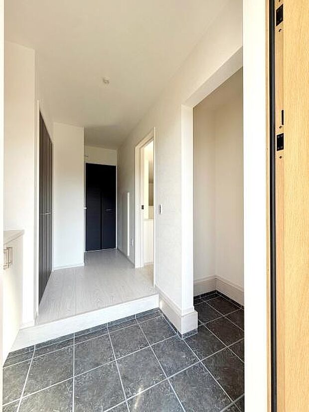 玄関の広々としたスペースが印象的です。明るい色合いの壁と床が空間をより開放的に感じさせます。収納もしっかり備わっているので整理がしやすいです。清潔感のあるタイルがアクセントになっています。