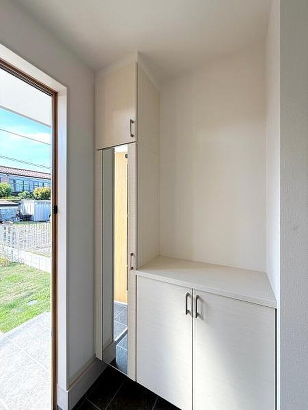 玄関には収納力のあるシューズボックスが設置されています。明るい採光があり開放感を感じられる空間です。ミラー付きで身だしなみも手軽に整えられます。床には落ち着いた色合いのタイルが使われています。