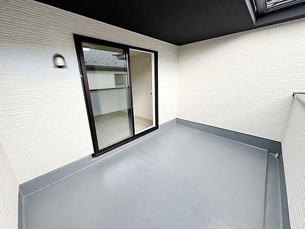 開放感のある広々としたバルコニーです。壁と床の色合いが明るい雰囲気を演出しています。スライドドアから室内への出入りがしやすい設計です。照明付きで夜間の利用にも便利です。屋根があるため雨天時も安心です。