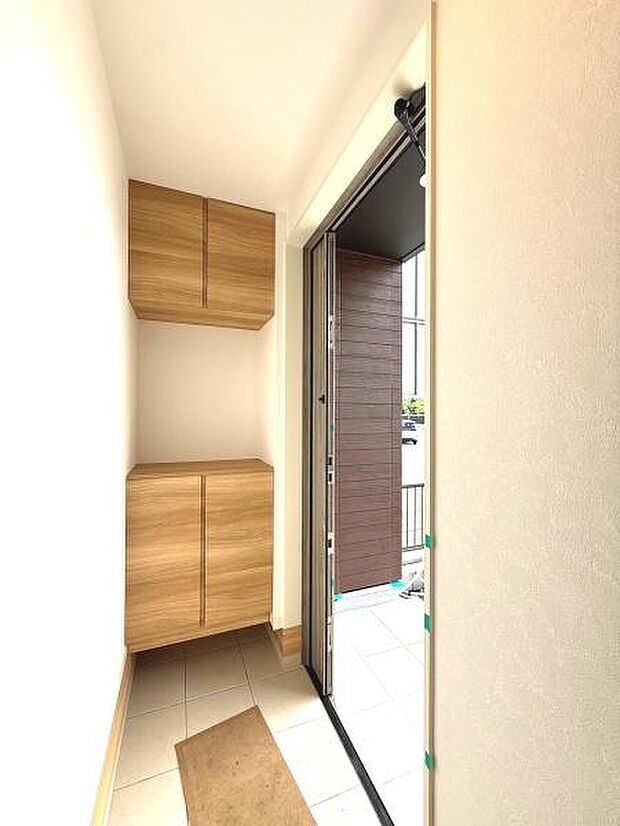 木目調の収納が設置された玄関です。明るい日差しが差し込む空間で清潔感があります。床はタイル張りで掃除のしやすさも特徴です。収納スペースも確保されており玄関まわりがすっきりと整えられます。