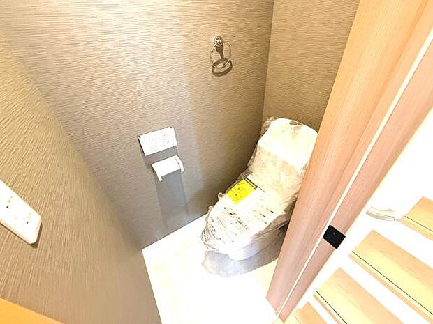 シンプルなデザインで日常使いに適したトイレです。ペーパーホルダーやタオルリングも設置されています。落ち着いた色合いの壁で空間が引き締まっています。出入口が階段近くにありアクセスが良好です。