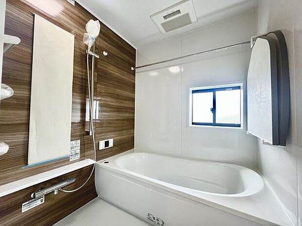 木目調のパネルがアクセントとなった落ち着いた雰囲気のバスルームです。浴槽は足を伸ばせる広さがあり窓から自然光も入ります。壁付けのミラーと収納棚も使いやすい仕様です。