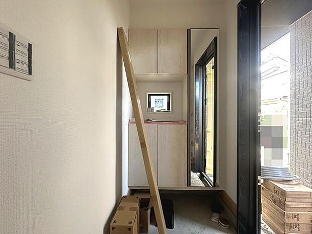 玄関には明るい光が差し込み開放感があります。全身鏡付きの収納が設置されており身支度がしやすいです。壁面にはインターホンが設置されています。木目調の収納と白い壁が調和しすっきりとした印象です。