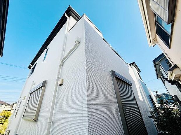 清潔感のある白い外壁が印象的です。シャッター付きの窓で安心感があります。しっかりとした造りが感じられる外観です。青空に映えるデザインが魅力です。モダンな印象の住宅です。
