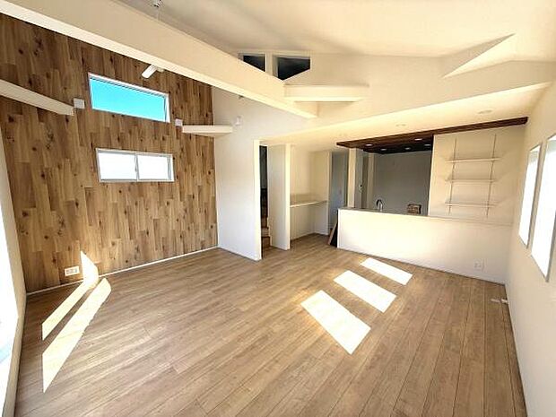 明るい日差しが差し込むリビングです。木目調のアクセントウォールが温かみを演出しています。天井のデザインも特徴的で開放感があります。窓の配置が工夫されており空間が広々と感じられます。