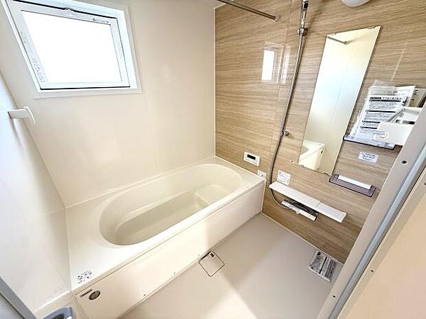 明るい窓付きのバスルームです。木目調のアクセントパネルが落ち着いた雰囲気を演出しています。浴槽やシャワー設備も使いやすい設計です。清潔感が感じられる空間になっています。