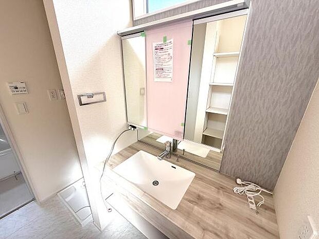 洗面台はシンプルで清潔感があります。大きめの鏡と広々としたカウンターが特徴です。収納棚もあり日用品を整理しやすい設計です。光が入る明るい空間で毎日の身支度が快適に行えます。
