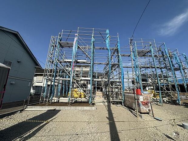 現在建築中の物件の様子です。しっかりとした足場が組まれています。工事車両が敷地内に停車できるスペースも確保されています。周辺には住宅が立ち並んでいます。