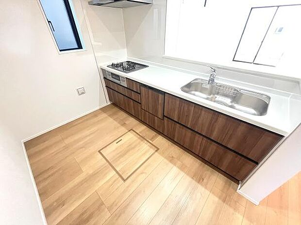 窓からの光が広がる明るいキッチンです。木目調の扉が温かみを感じさせるデザインです。広々とした作業スペースが確保されています。使いやすい配置で日々の調理もスムーズです。