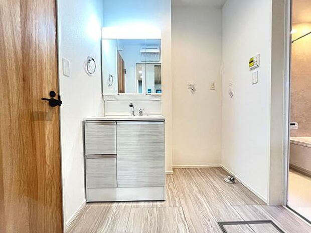 明るい照明が特徴的な洗面台です。収納スペースが豊富ですっきりとしたデザインが魅力的です。床材と一体感のある落ち着いた雰囲気の空間です。水回りへのアクセスもスムーズにできます。