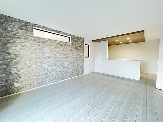 グレーのアクセントウォールが印象的なリビングです。天井の木目調が空間に温かみを感じさせます。スリット窓で室内が明るくなっています。開放感を感じるレイアウトです。