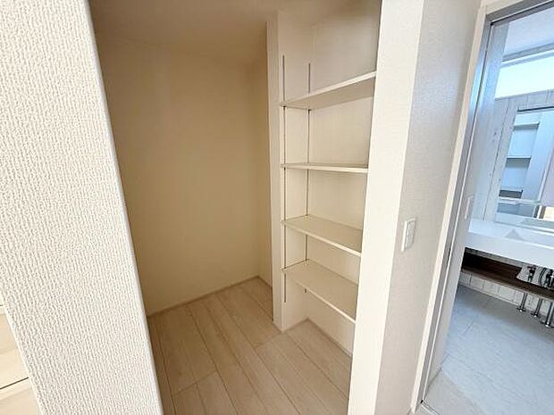 奥行きのある収納スペースが備わっています。可動式の棚が設置されており用途に応じて調整が可能です。明るい色合いのフローリングと壁ですっきりとした印象です。隣接する洗面室との動線も良好です。