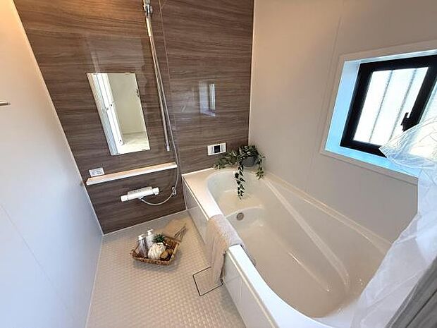 清潔感のあるバスルームが特徴です。木目調の壁面が落ち着いた雰囲気を演出しています。大きめの窓があり換気もしやすい設計です。ゆったりとした浴槽でリラックスできます。収納棚や鏡も備え付けられています。