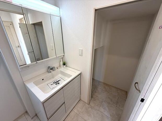 洗面台は広めのカウンターで使い勝手が良い設計です。三面鏡が備わっており収納スペースも豊富です。隣接する収納スペースがあり日常の動線もスムーズです。清潔感のある白基調の空間でお手入れも簡単です。