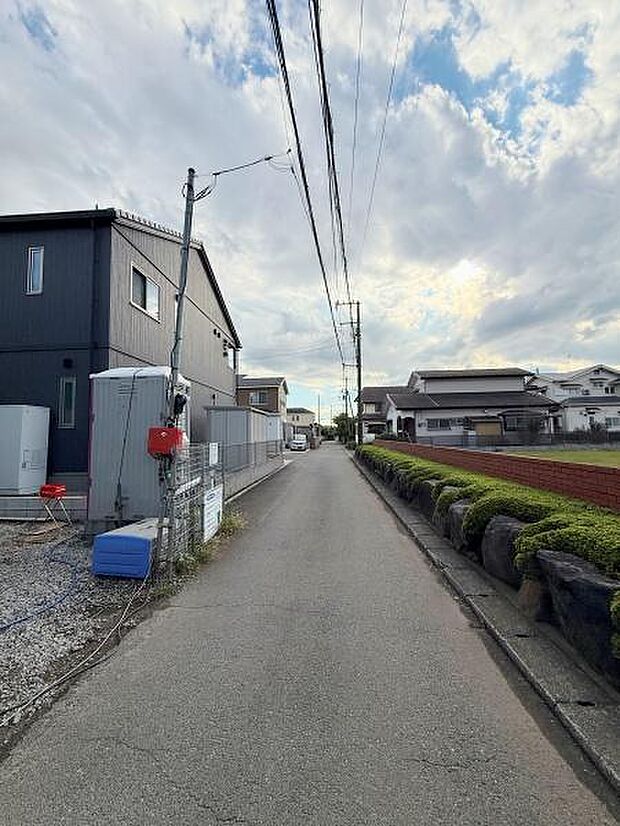 周辺には落ち着いた住宅が並び前面道路はすっきりとした印象です。片側には生垣と石積みが整然と配置されています。道路幅は車の通行にも十分な広さです。周囲の景観も開放的で日当たりにも恵まれています。
