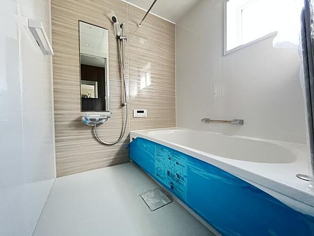 明るい印象のバスルームで浴槽は広々とした設計です。壁面にはグレーのパネルが使用され清潔感があります。窓から自然光が差し込みすっきりとした空間を演出しています。