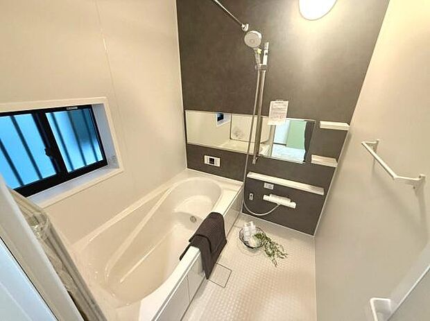 窓があり換気や採光に配慮されたバスルームです。ゆったりとした浴槽で快適に使用できます。落ち着いた色合いの壁面パネルが空間に調和を与えています。収納棚や大きめのミラーも備わっています。