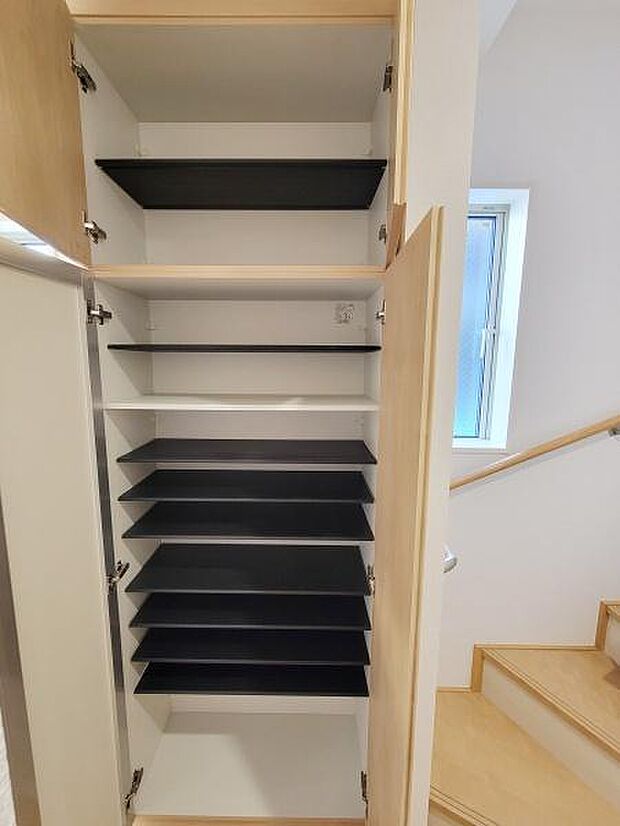 シンプルなデザインの収納スペースです。棚の高さが異なり使い分けがしやすい仕様となっています。階段付近に位置しているため動線にも配慮されています。扉付きで中身を隠せる構造です。