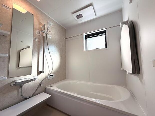 大きな窓があり明るい自然光が差し込むバスルームです。白を基調とした清潔感あふれるデザインです。鏡や収納棚が便利に配置されています。浴槽とシャワーエリアがゆとりのある設計です。換気設備が整っています。
